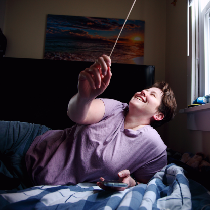 Person laying on their bed, with a joyful expression, holding a taut string in their hand.